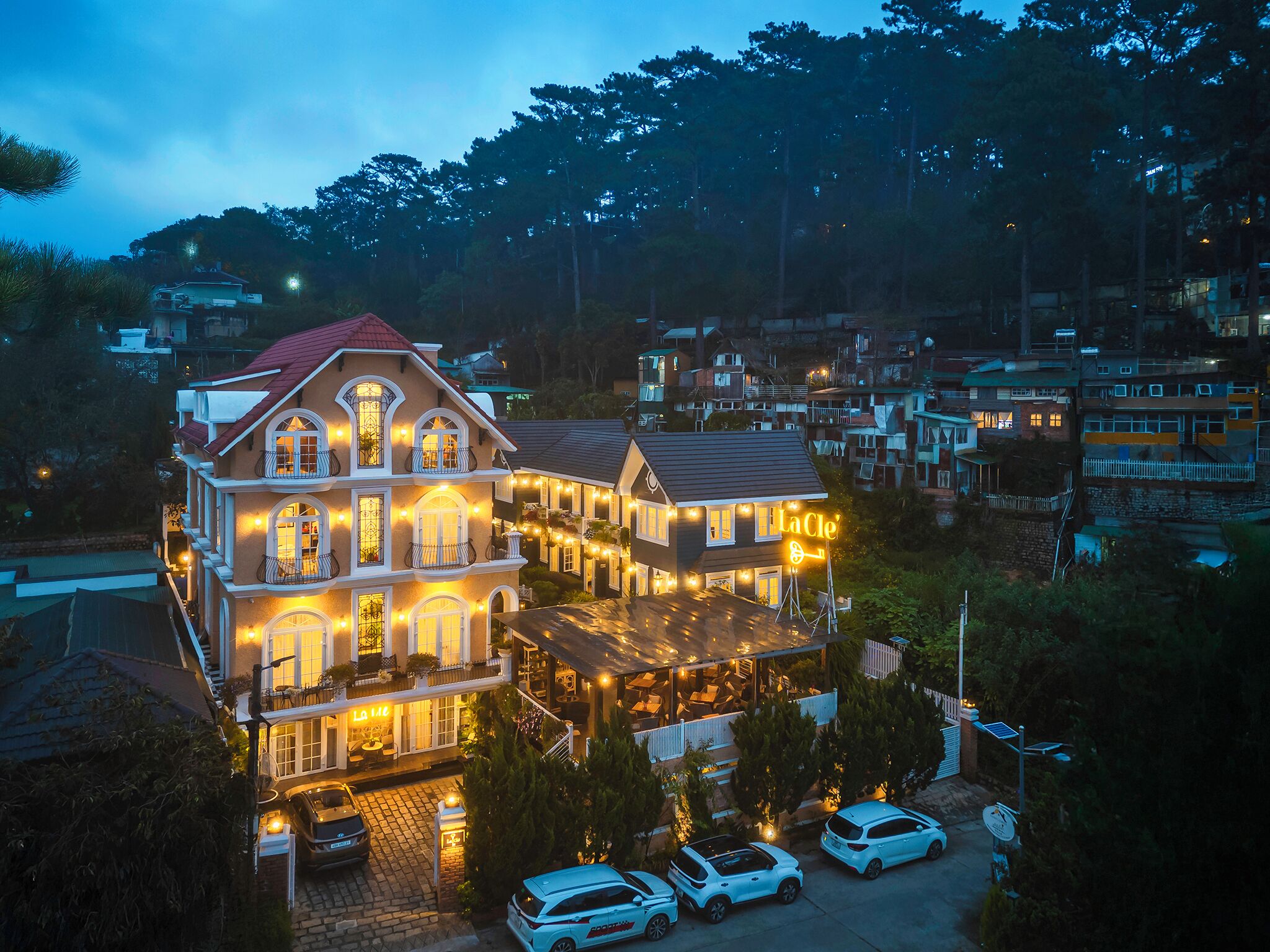 Un hotel de varios pisos con techo rojo, múltiples balcones y luces de cadena.