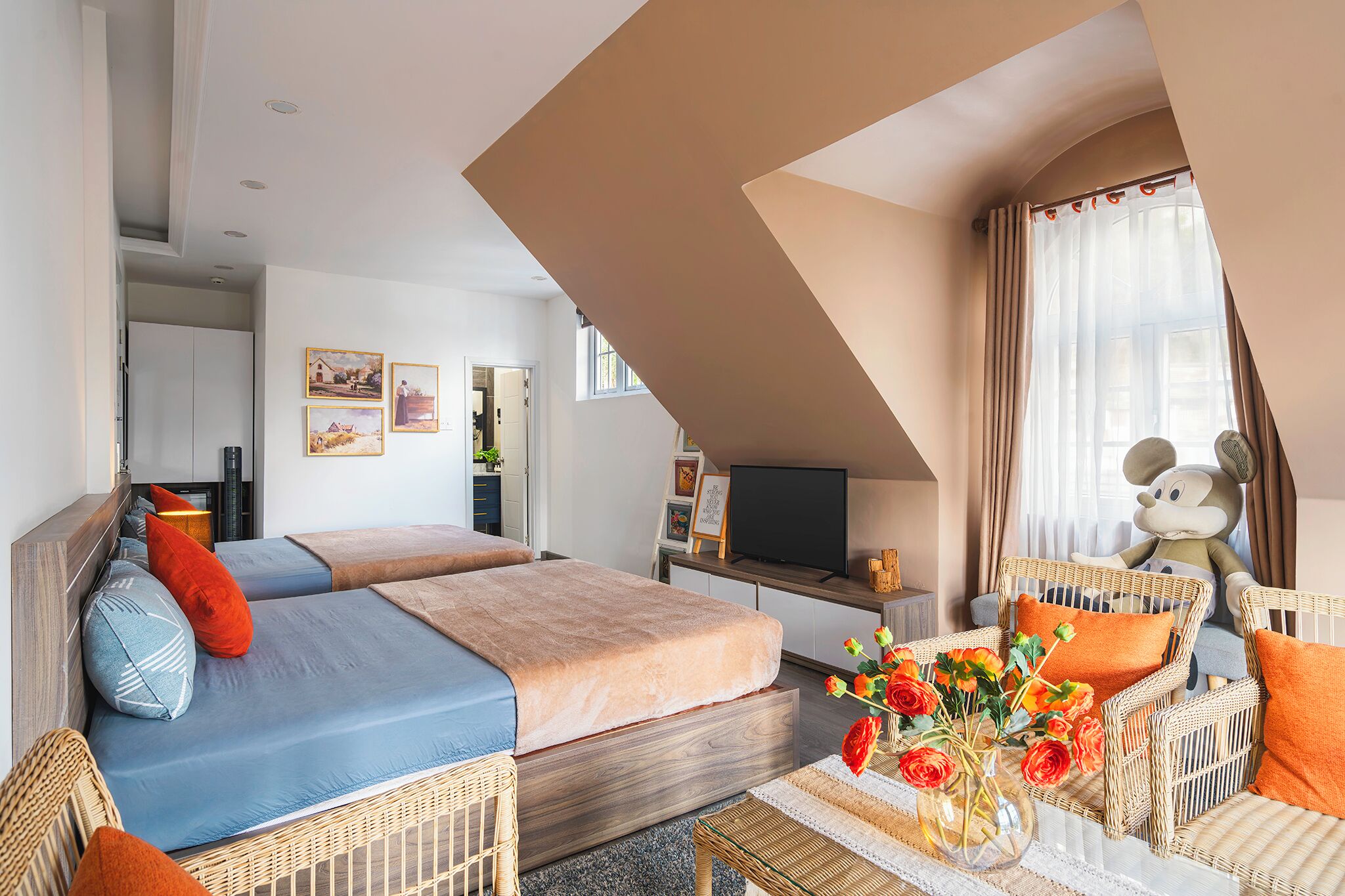 A hotel room with a bed, a TV, wicker furniture, and a Mickey Mouse statue.