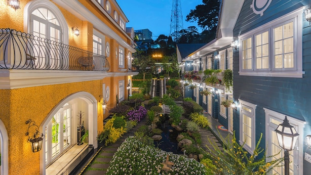 Une ruelle étroite avec un petit jardin, une fontaine et des bâtiments dotés de balcons et de fenêtres.