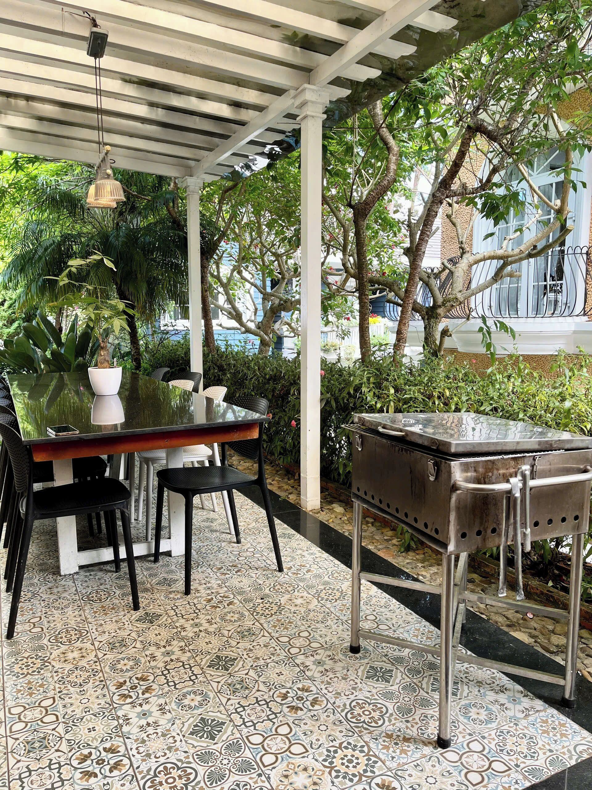A covered patio with a table, chairs, a grill, and potted plants.