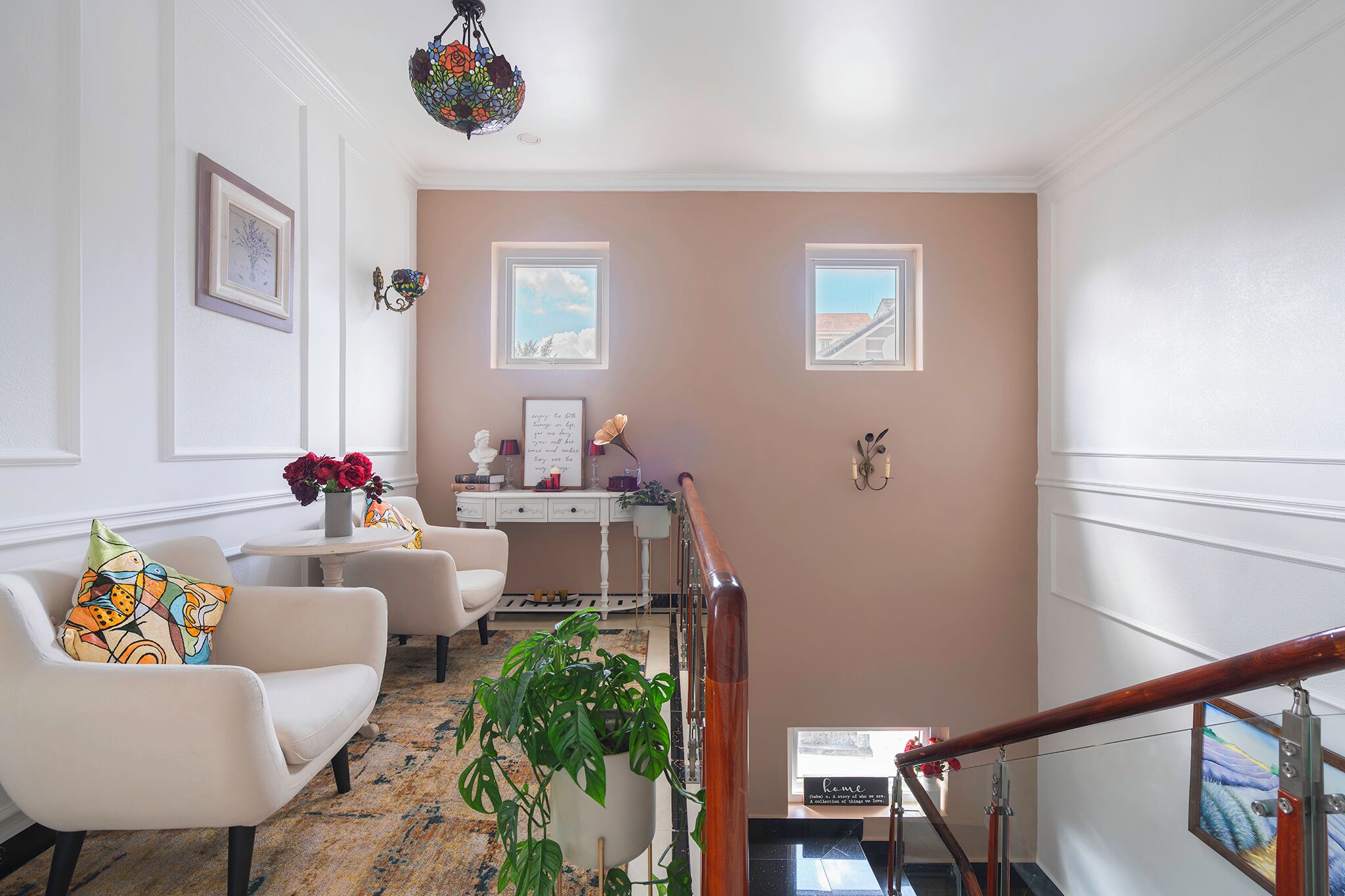 Un salón bien iluminado con una escalera, un escritorio con un jarrón de flores y vistas al exterior a través de una ventana.