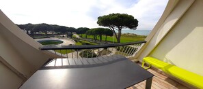 Ein Balkon mit Blick auf eine angelegte Grünfläche, einen Pool und ein Gewässer.