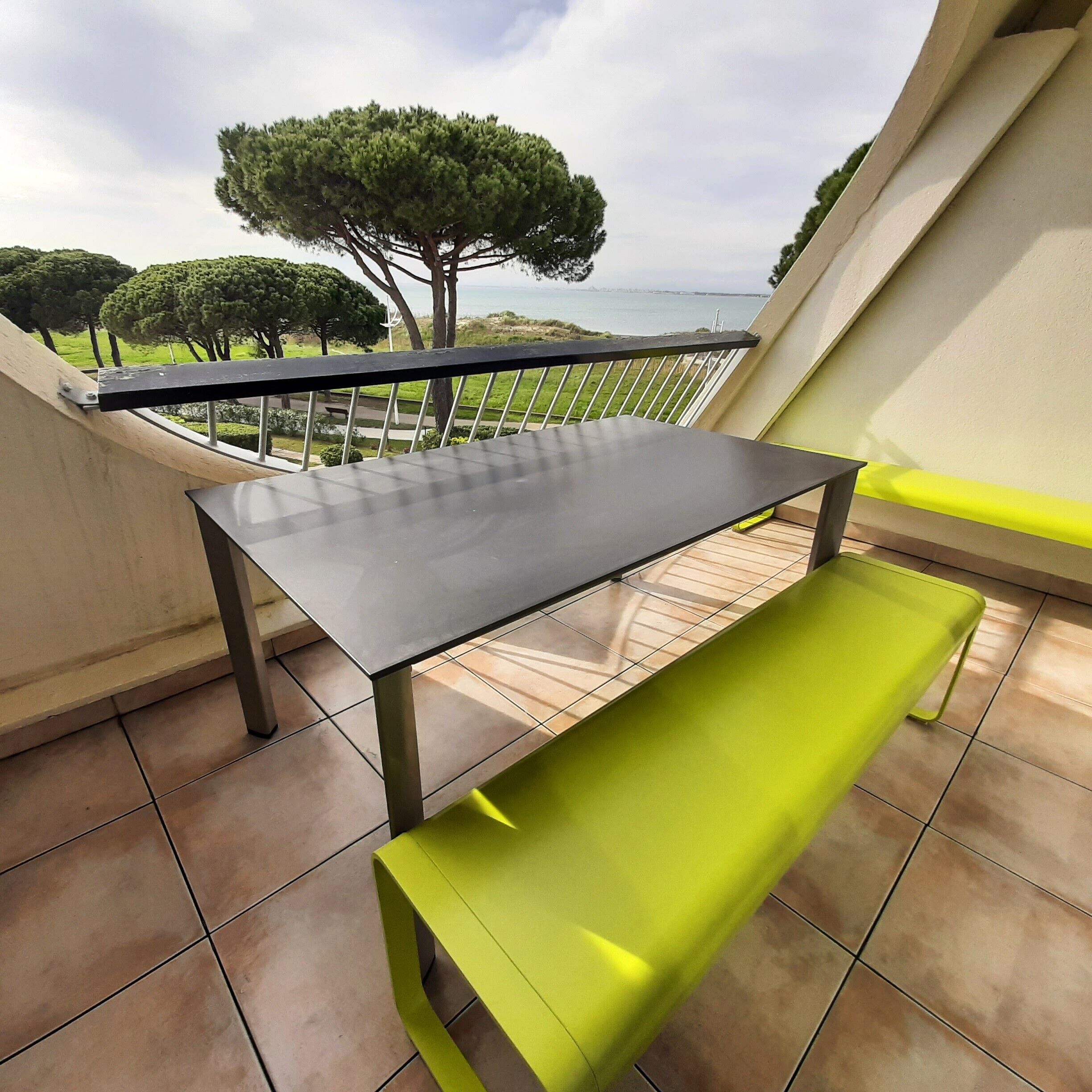Een balkon met een tafel en een bank, met uitzicht op een grasveld en bomen.