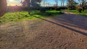 A gravel path leading through a rural landscape with trees and a clear sky.