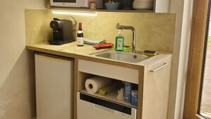 A compact kitchenette with a microwave, coffee maker, sink, and storage drawers.
