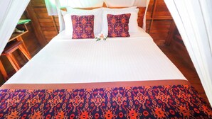 Un lit avec du linge de lit blanc, deux coussins à motifs et un arrangement floral.