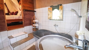 Une salle de bain avec une grande baignoire, un lavabo, un miroir et un lit en bois doté d’un baldaquin.