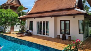 A modern house with a swimming pool, large windows, and a traditional Thai roof.