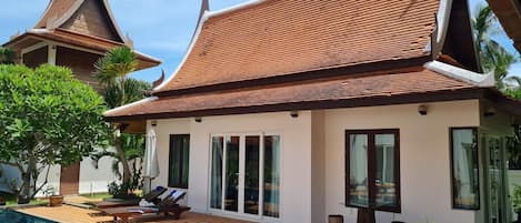 A modern house with a swimming pool, large windows, and a traditional Thai roof.