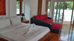 A hotel room with a bed, a red sofa, a nightstand with a lamp, and a painting on the wall.