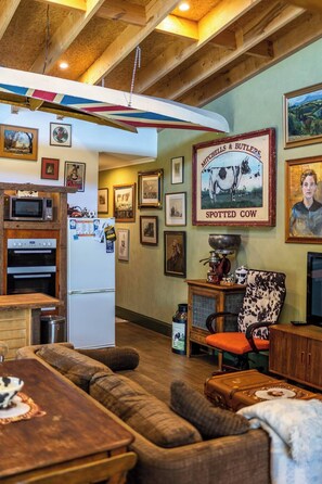 Een gezellige woonkamer met een houten plafond, een groot lijstwerkposter van een koe en een fauteuil in vintage stijl.
