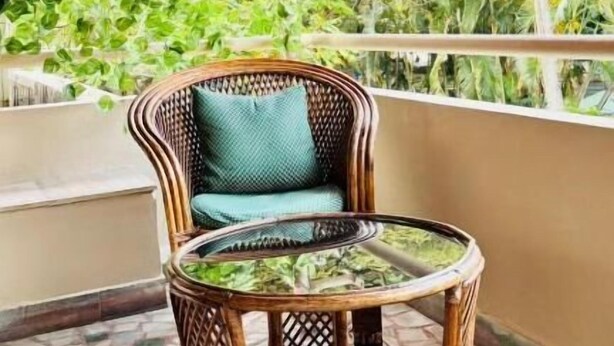A wicker chair with a glass table on a tiled balcony with a view of greenery and pink flowers. - SCARLET'S INN (Kochi)