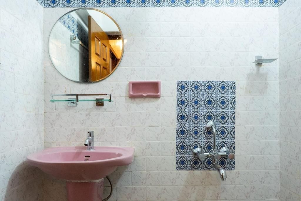 A bathroom with a pink sink, a mirror, a shower, and patterned tiles.