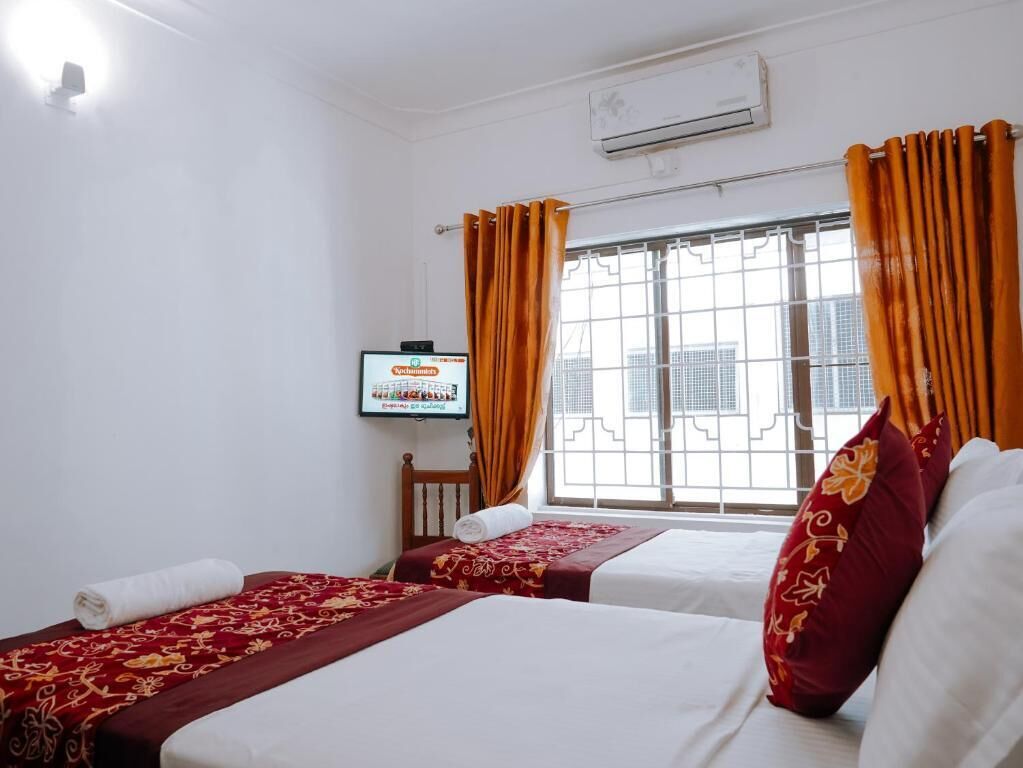 A hotel room with two beds, a television, and a window with curtains.