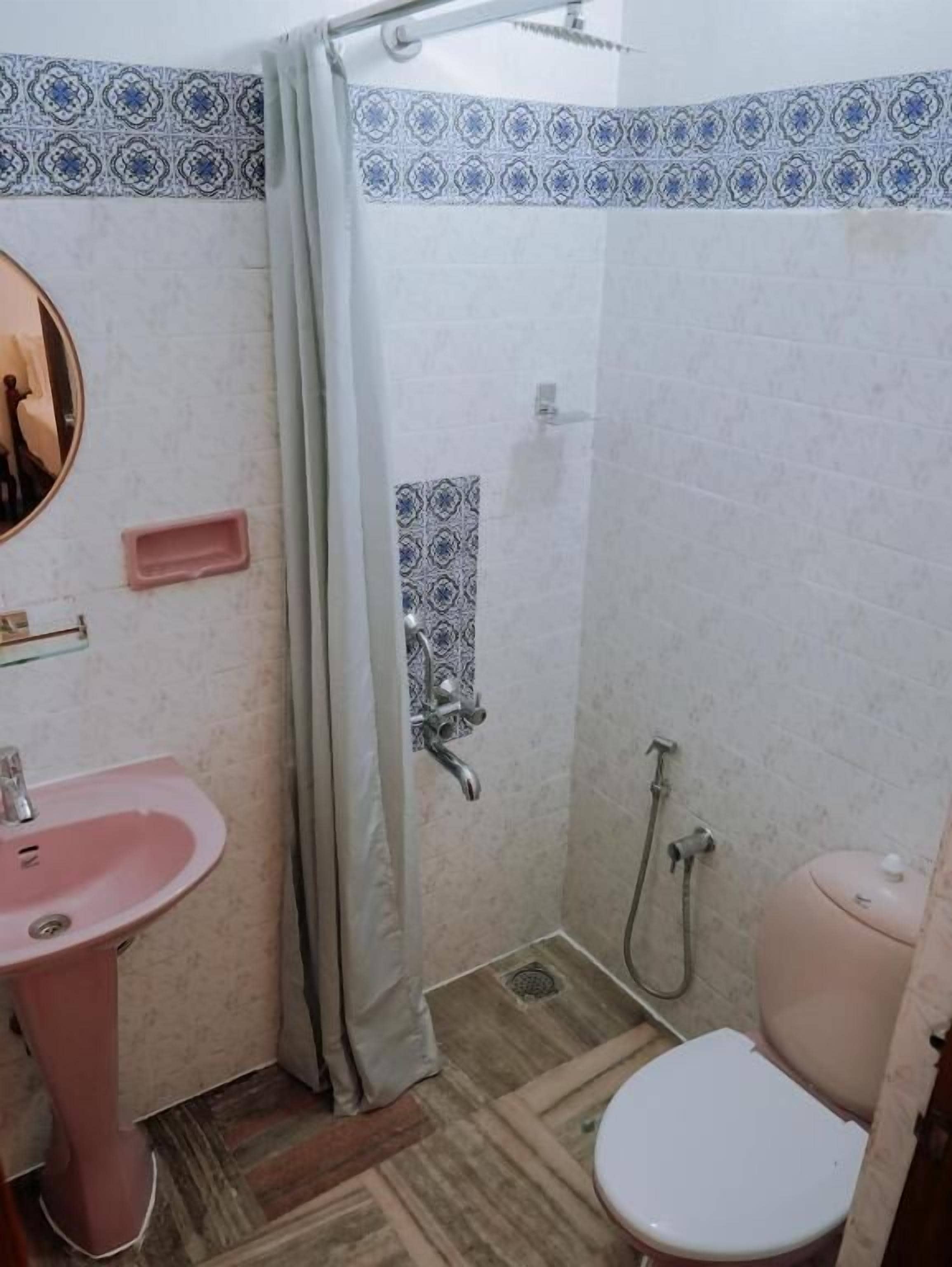 A small bathroom with a pink sink, a toilet, and a shower area.