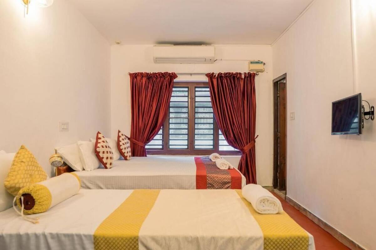 A hotel room with two beds, red curtains, a TV, and an air conditioning unit.