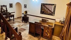 A spacious living area with a wooden staircase, a dining table, and a ceiling fan. - SCARLET'S INN (Kochi)