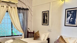 A hotel room with two single beds, a ceiling fan, an air conditioning unit, a window with curtains, and wall-mounted artwork. - SCARLET'S INN (Kochi)