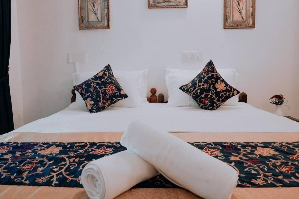 A neatly made bed with floral-patterned pillows and a rolled white towel in front.