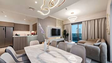 A modern living room with a marble dining table, grey sofas, and a TV mounted on the wall.