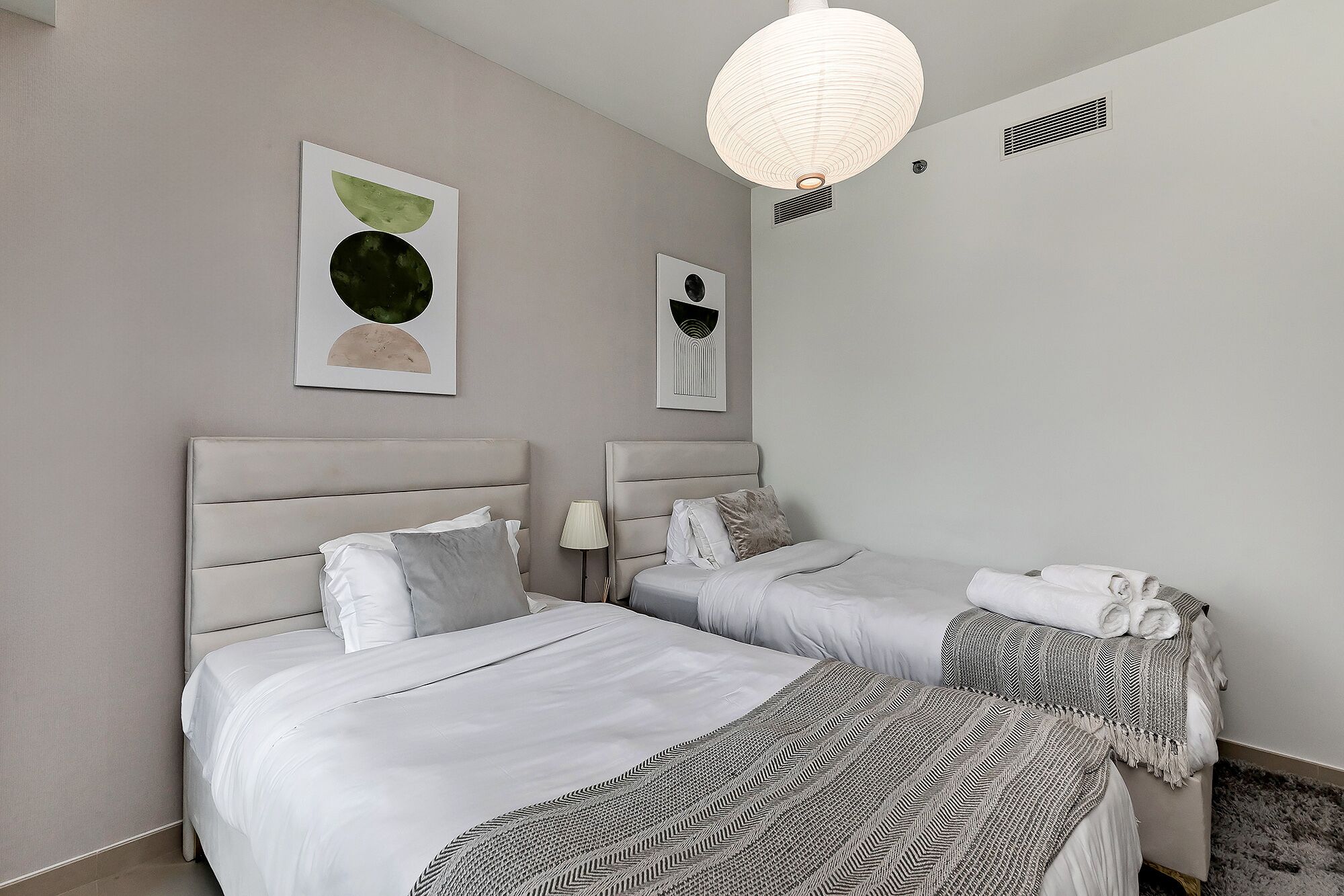 A hotel room with two beds, a ceiling light, and artwork on the walls.