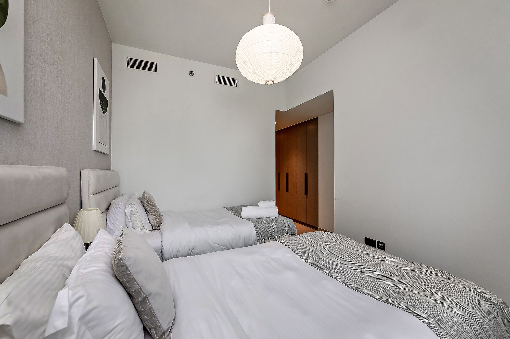 A modern bedroom with a bed, bedside tables, a hanging light fixture, and a wardrobe.