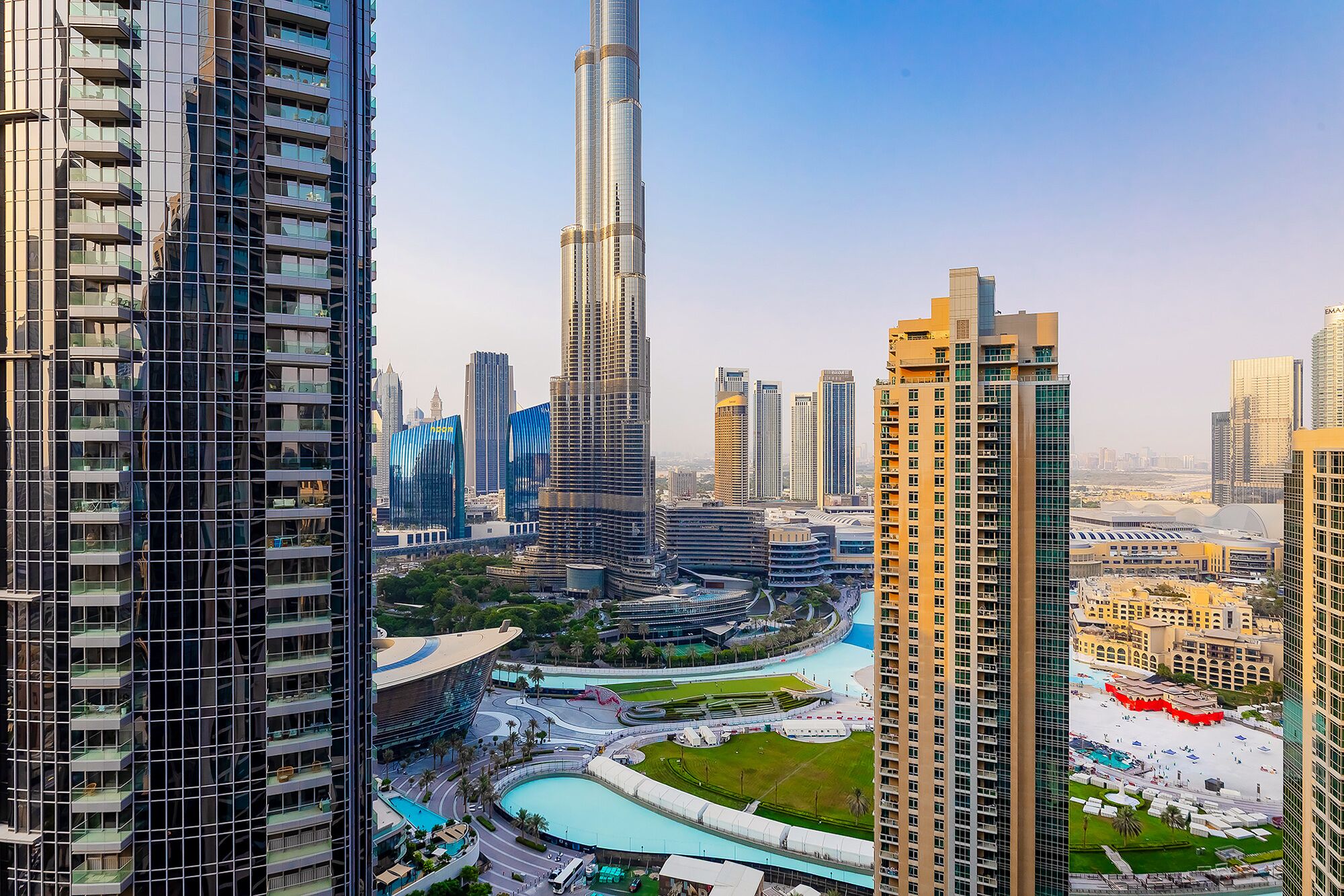 A high-rise building with a curved facade, surrounded by other tall buildings and a central plaza with a pool.