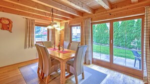 Una sala da pranzo con pannelli in legno, un tavolo grande e sedie, ampie finestre con tende e vista su un paesaggio verde.