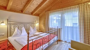 Camera in una baita di legno, con un letto con struttura in metallo, biancheria bianca e una coperta rossa.