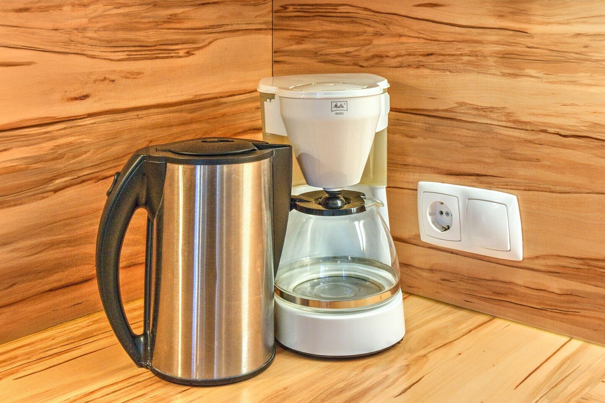 A stainless steel coffee pot and a white coffee maker on a wooden countertop.