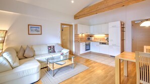 A modern living room with a white sofa, glass coffee table, and wooden dining table. - Apartment in Wildschönau – Vicky Apartment (Wildschönau)