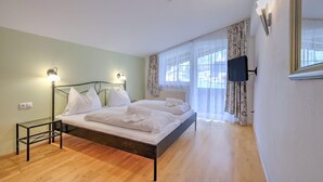 A bedroom with a bed, bedside tables, a flat-screen TV, and a window with curtains. - Apartment in Wildschönau – Vicky Apartment (Wildschönau)
