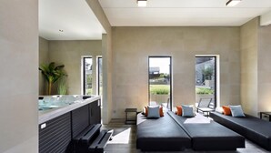 Ein moderner Wellnessraum mit einer großen Badewanne, einer Schlafcouch und Blick ins Freie.