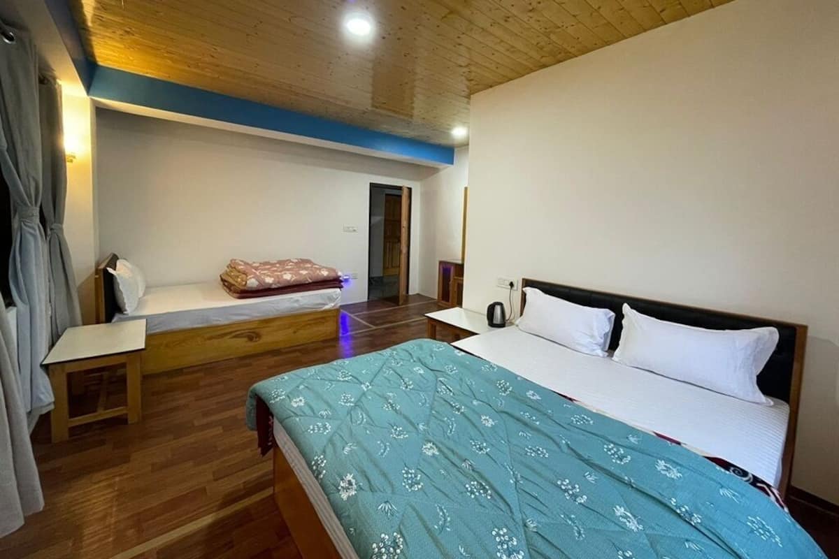 A bedroom with a wooden ceiling, a bed with a blue patterned bedspread, a bedside table, and a small desk.