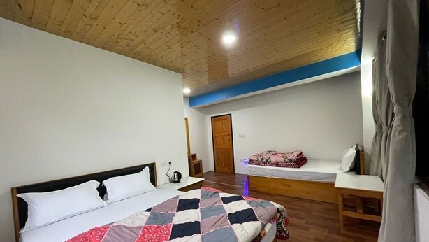 Un dormitorio con techo de madera, una cama con colcha, una mesita de noche y un banco con manta.