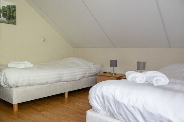 Une chambre avec deux lits, une table de chevet avec une lampe et un interrupteur fixé au mur.