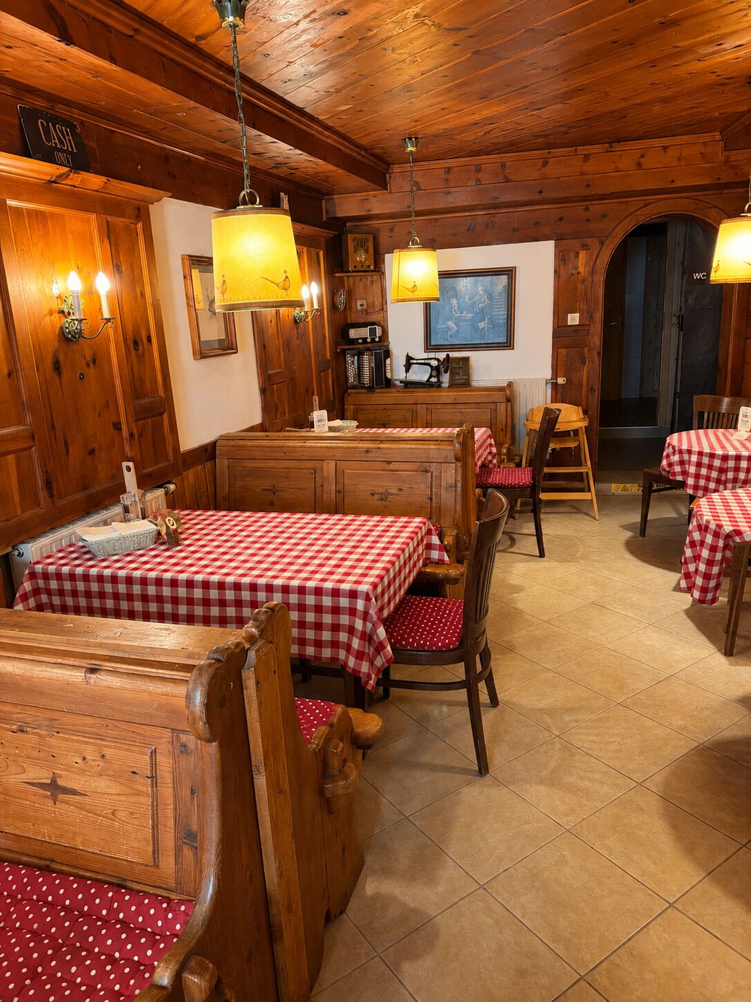 A rustic dining area with wooden tables and benches, a cash-only sign, and a WC sign.