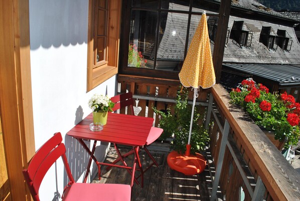 Un balcon avec une table rouge, des chaises rouges, un parasol jaune et des fleurs rouges.
