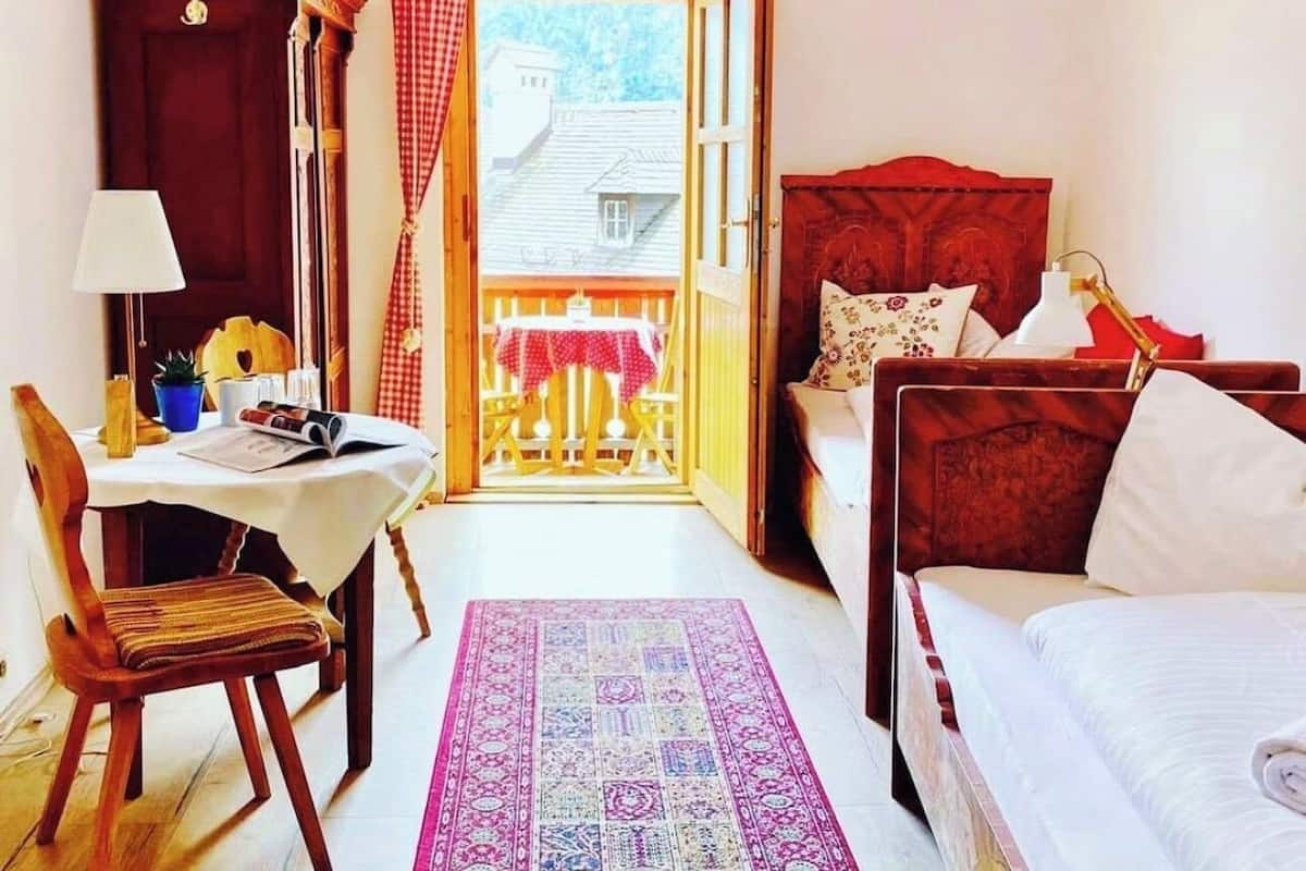 Een gezellige kamer met een bed, een bureau met stoel, een klein tafeltje met stoel en uitzicht op een balkon met tafel en stoelen.