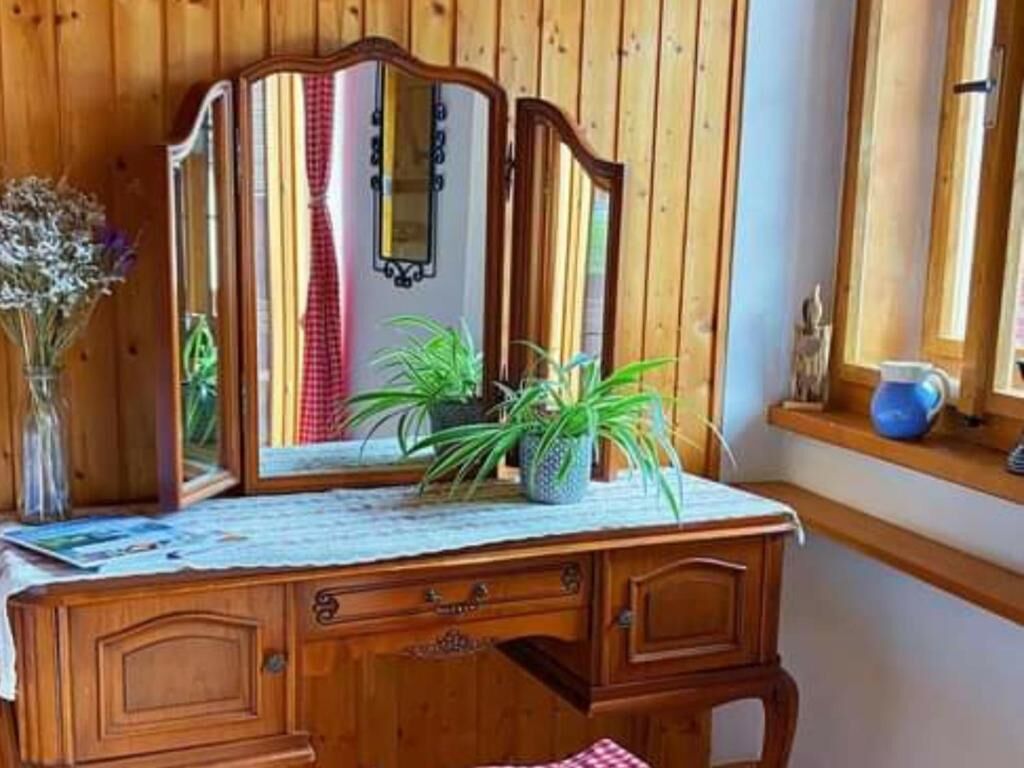 Ein hölzerner Kommode mit Spiegel, eine Vase mit Trockenblumen und ein Fenster mit Blick ins Freie.