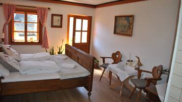Un dormitorio con cama de madera, una mesa de comedor, dos sillas, una ventana con cortinas y un cuadro en la pared.
