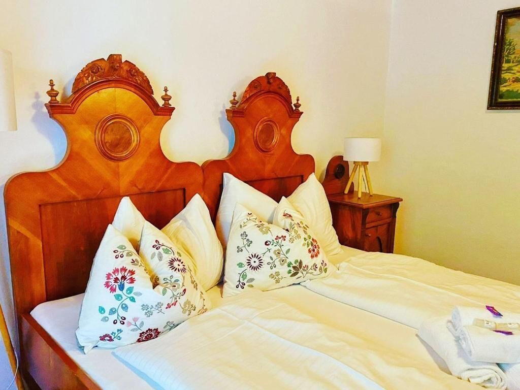 Una cama bien hecha con almohadillas florales, cabecera de madera y mesita de noche con lámpara.