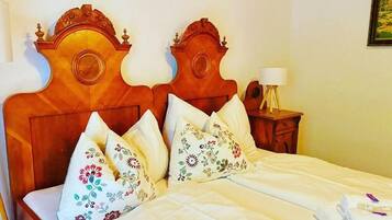 Ein ordentlich bezogenes Bett mit floralen Kissen, einem Holzkopfschild und einem Nachttisch mit Lampe.