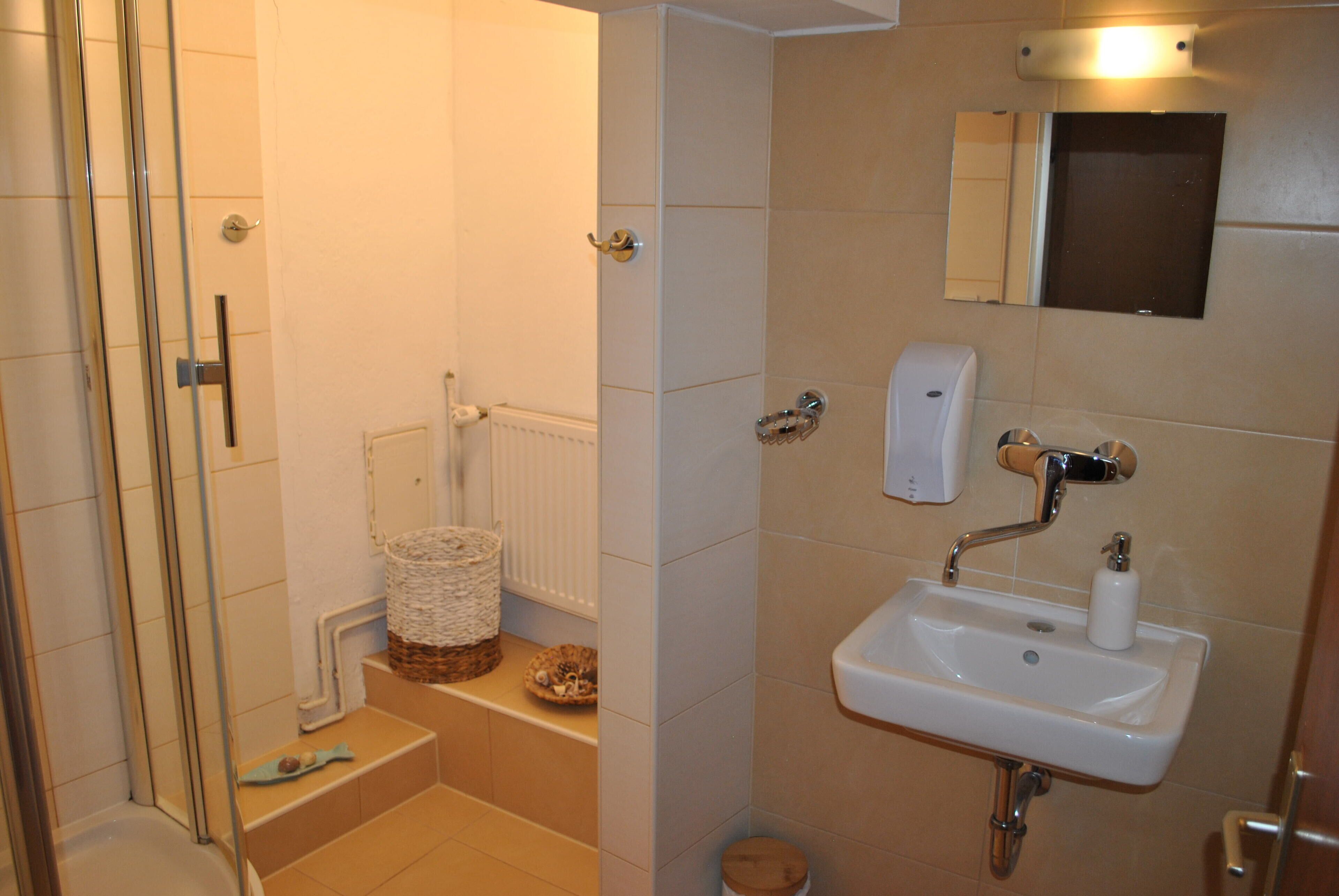 A bathroom with a shower, a sink, a toilet, and a small basket on the floor.