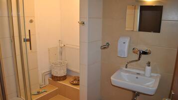 A bathroom with a shower, a sink, a toilet, and a small basket on the floor.