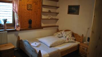 Une petite chambre à coucher accueillante, avec un lit en bois, une table de chevet, une commode, une fenêtre ornée d’un rideau à carreaux et une étagère murale décorative.