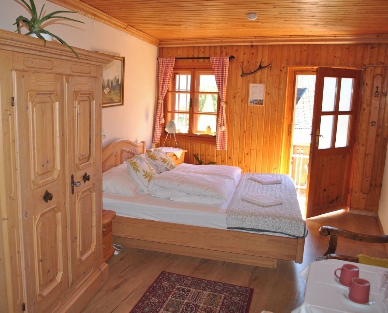 Una habitación de madera con cama, un armario, una ventana con cortinas y una puerta.