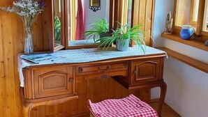 A wooden dresser with a mirror, a small stool with a checkered cloth, and a vase with dried flowers. - Pension Leopoldine (Hallstatt)