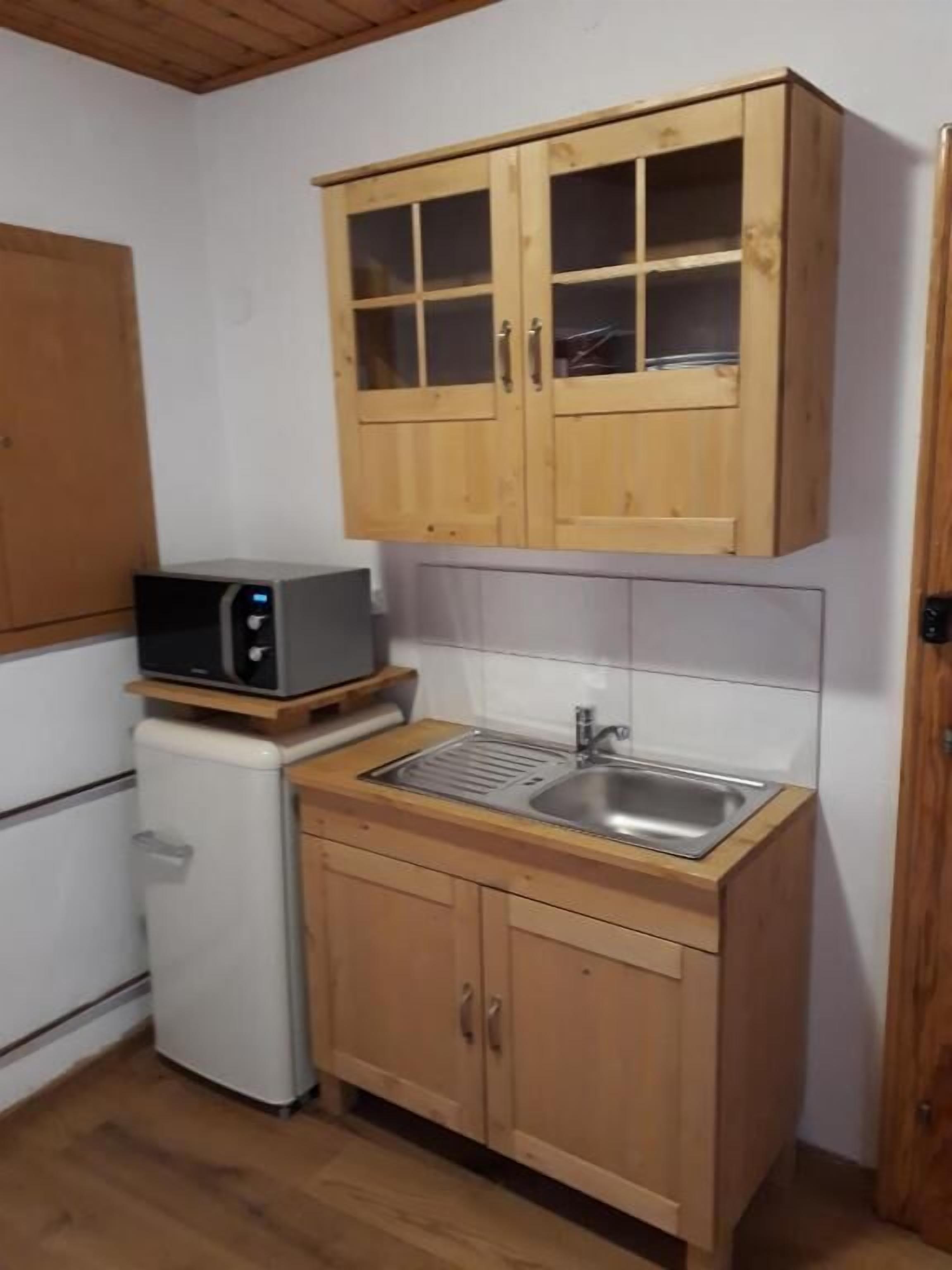 A compact kitchen with wooden cabinets, a microwave, a sink, and a refrigerator.