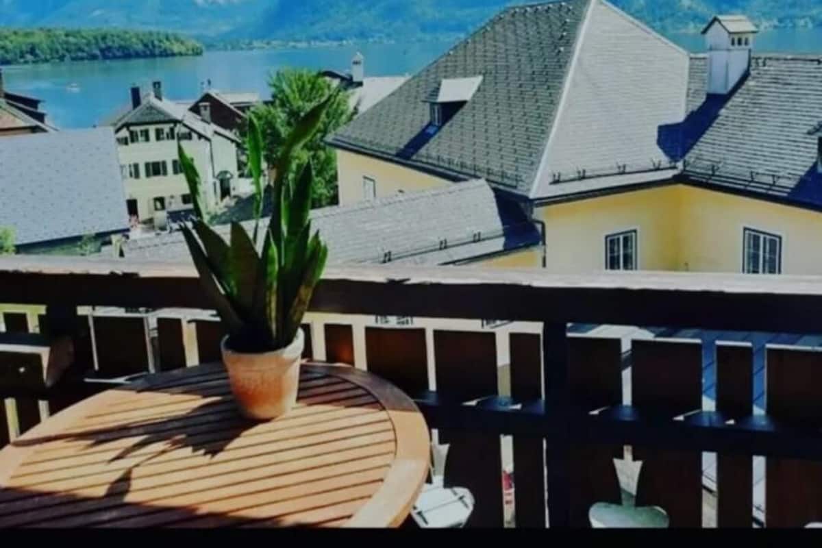 Een balkon met een bloempot, met uitzicht op een bergachtig landschap en een meer.
